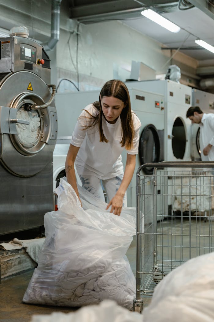Woman handling laundry in a commercial washing facility, focusing on tasks and efficiency.